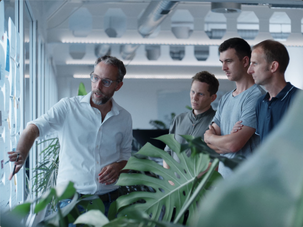 Vier Teammitglieder von Helga stehen vor einer Wand besprechen die aufgehängten Entwürfe.