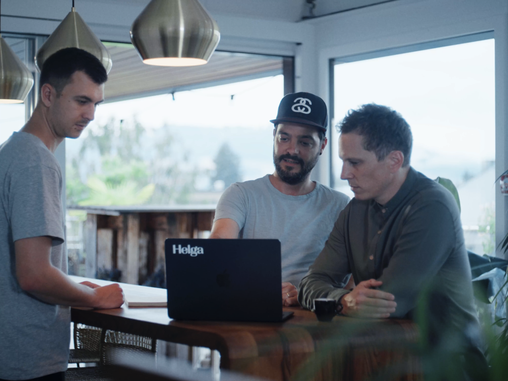 Zwei Teammitglieder von Helga stehen mit einem Laptop an der Bar und besprechen ein Projekt.